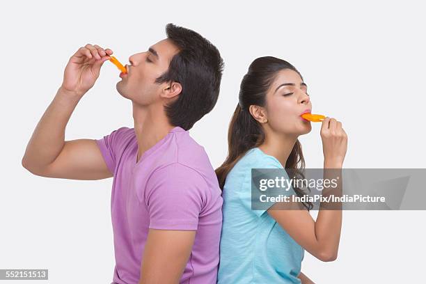 young couple enjoying orange ice lollies over white background - wassereis mit orangengeschmack stock-fotos und bilder