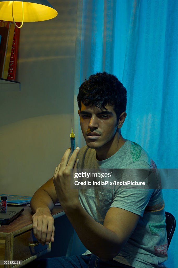 Young drug addict holding syringe at home