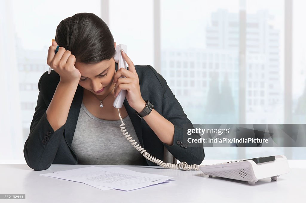 Worried businesswoman answering telephone at office desk