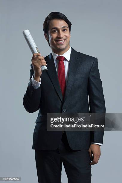 portrait of smiling businessman holding newspaper over gray background - rolled newspaper stock pictures, royalty-free photos & images