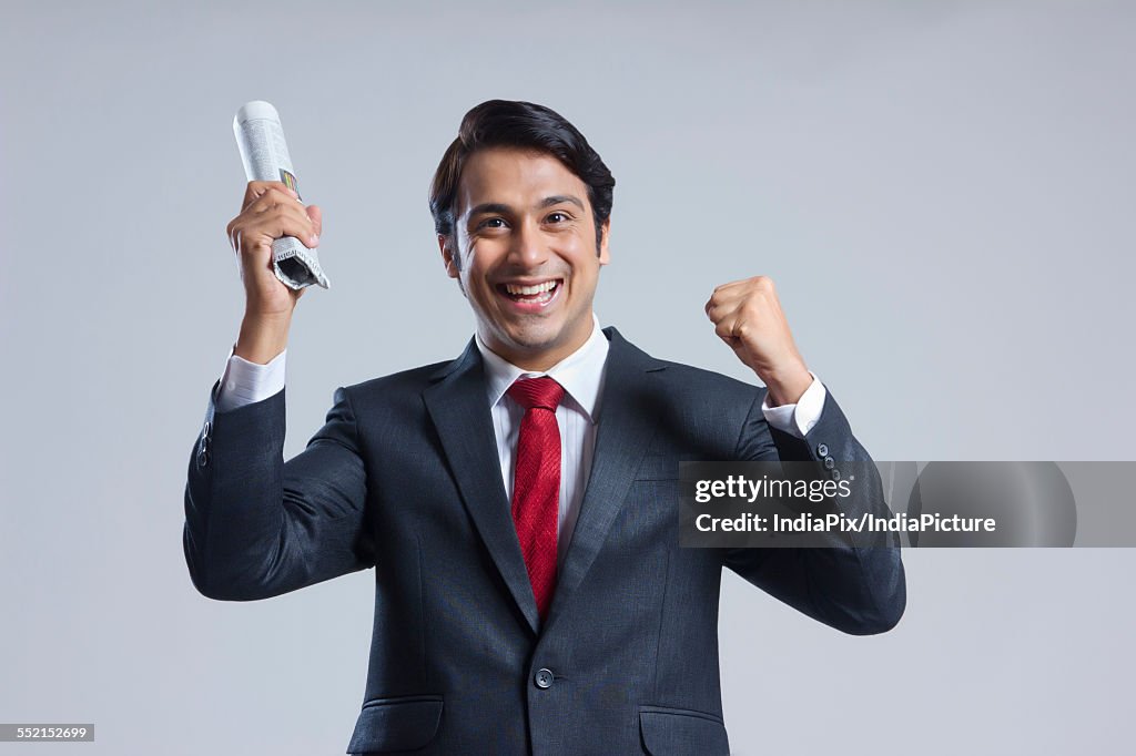 Portrait of successful businessman holding newspaper against gray background