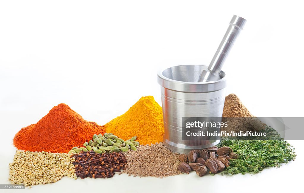 Mortar and pestle with variety of spices over white background