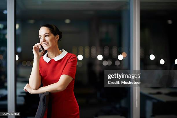 woman talking on the phone in office at night - red dress stock pictures, royalty-free photos & images