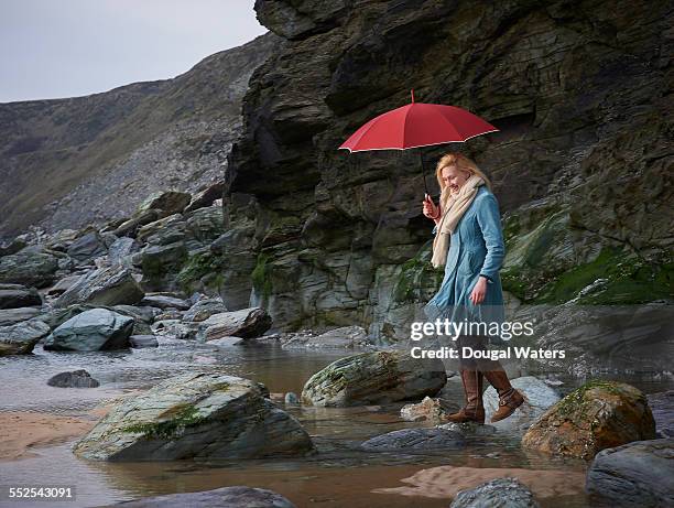 woman walking on rocky beach with umbrella. - long coat stock pictures, royalty-free photos & images