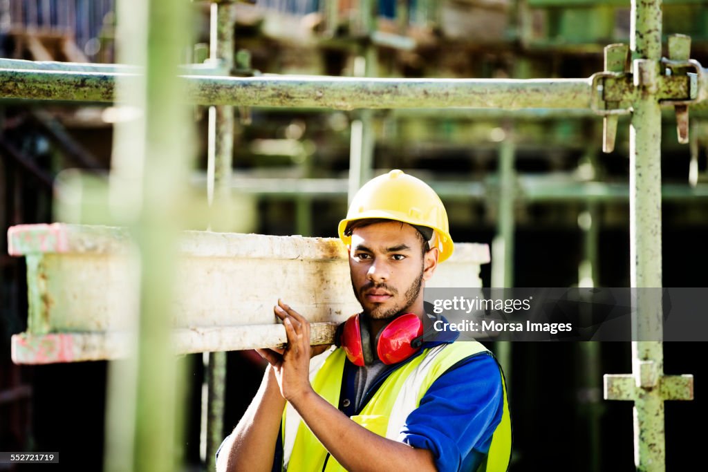 Trabajador de la construcción que lleva tablón en el sitio