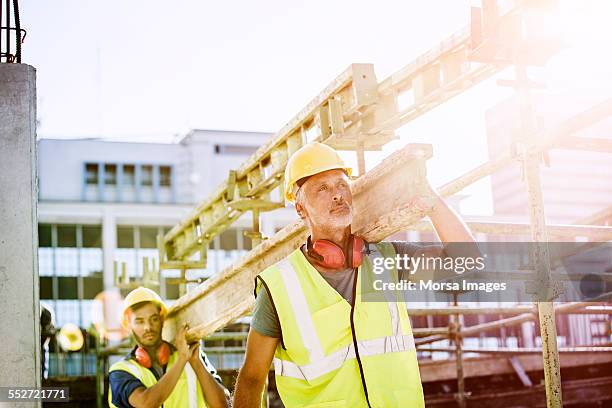 construction workers carrying plank at site - ouvrier du bâtiment photos et images de collection