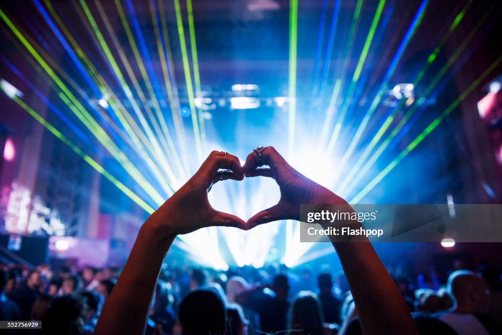 Woman making heart shape with hands at music event