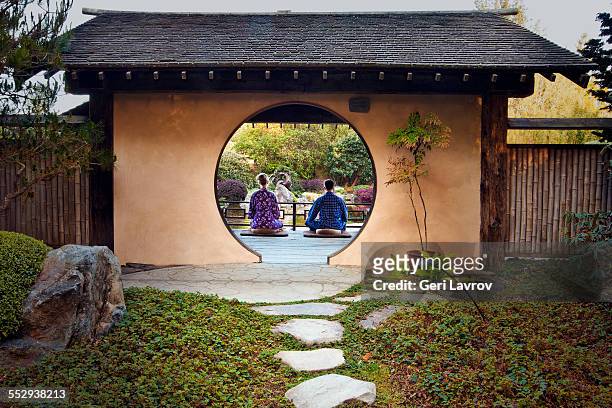 couple in robes meditating in a zen garden - lotuspositie stockfoto's en -beelden