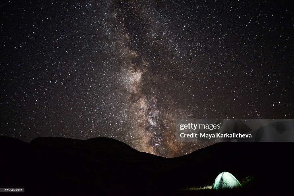 Milky way rises above illimunated tent in mountain