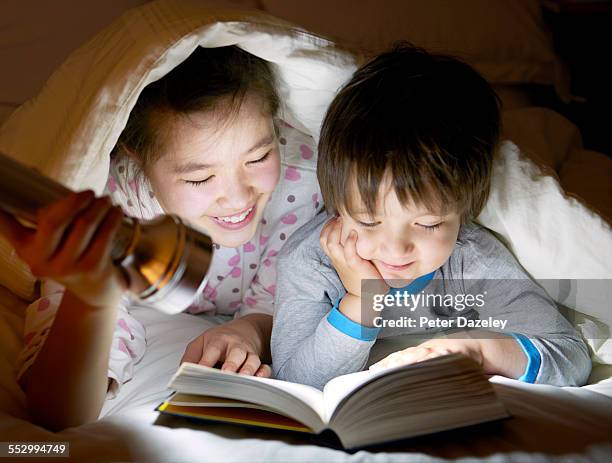 brother and sister reading under the covers - electric torch stock pictures, royalty-free photos & images