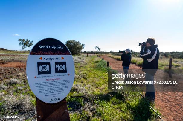 tourists photograph an area of uluru near an aboriginal sacred site despite a sign forbidding it. - area 51 stock pictures, royalty-free photos & images