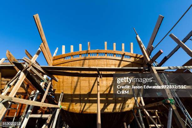 Timber and steel scaffolding supports the hull during handmade construction of an ancient timber dhow. Sur, Ash Sharqiyah Region, Gulf of Oman,...