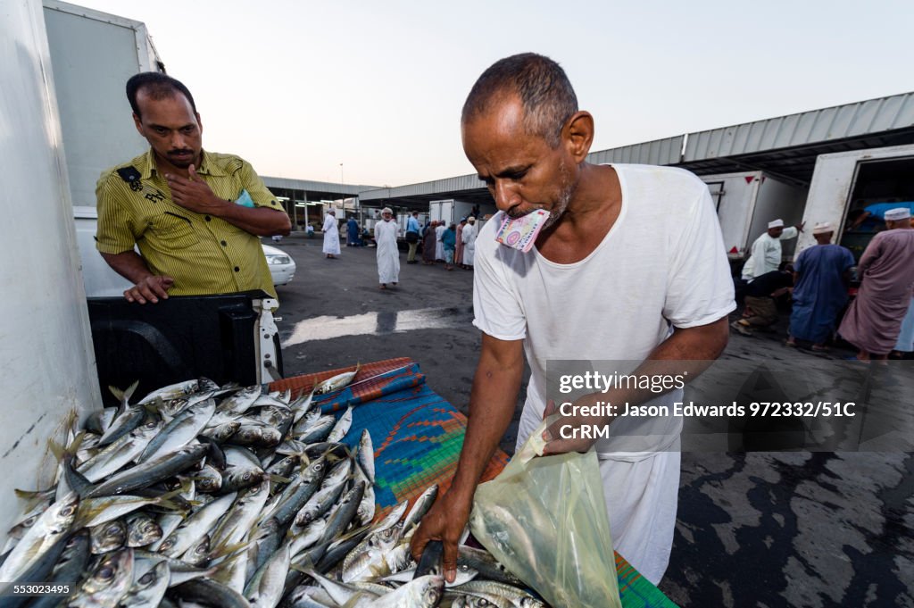 Two men haggle over a mound of sardine fish for sale in a fish market.