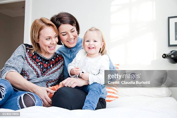 lesbian couple cuddling their daughter - leaninlgbt stock pictures, royalty-free photos & images