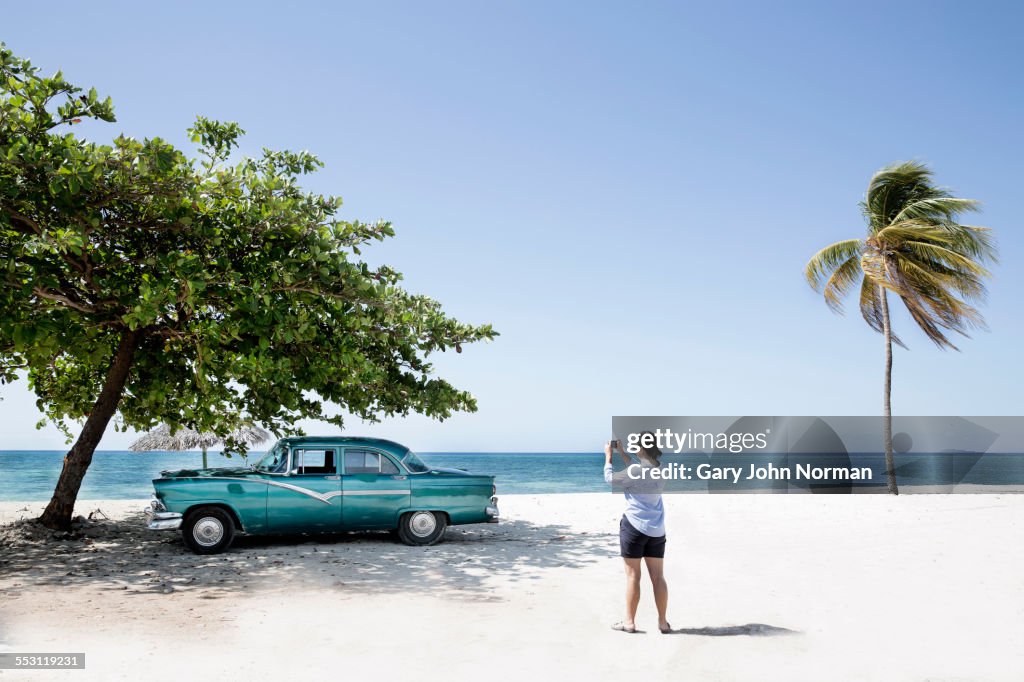Woman takes photo of American car on the beach.