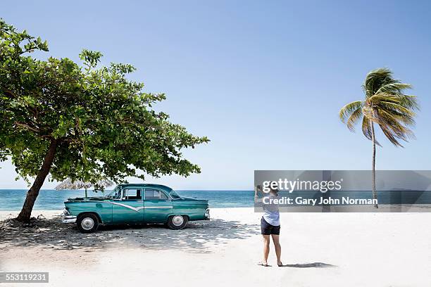woman takes photo of american car on the beach. - cuba car stock pictures, royalty-free photos & images