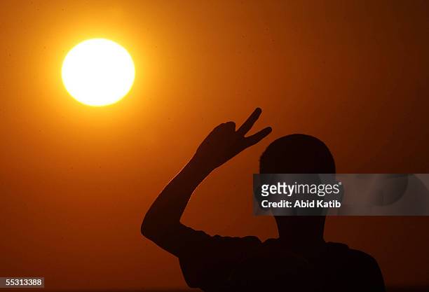 Palestinian boy gestures a V-sign as he looks at an Israeli tank open fire while guarding the border of the vacant Jewish settlement of Neve Dekalim...