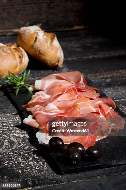 parma ham and black olives on chopping board, dark wood - jambon de parme photos et images de collection