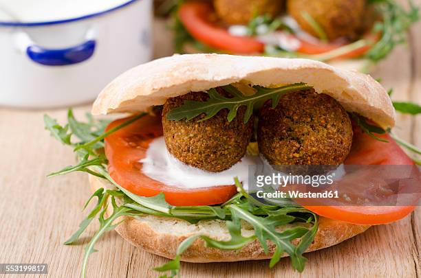 homemade falafel, tomato, yoghurt sauce, rocket and mint in pita bread on chopping board - pita bread stock pictures, royalty-free photos & images