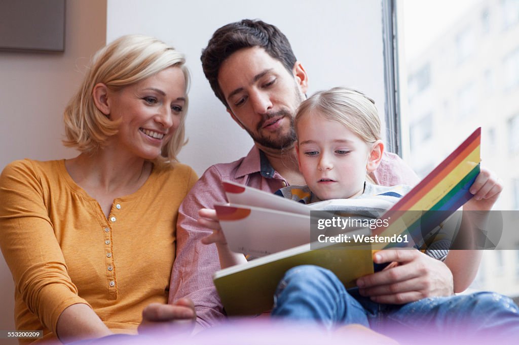 Father and mother reading picture book to daughter