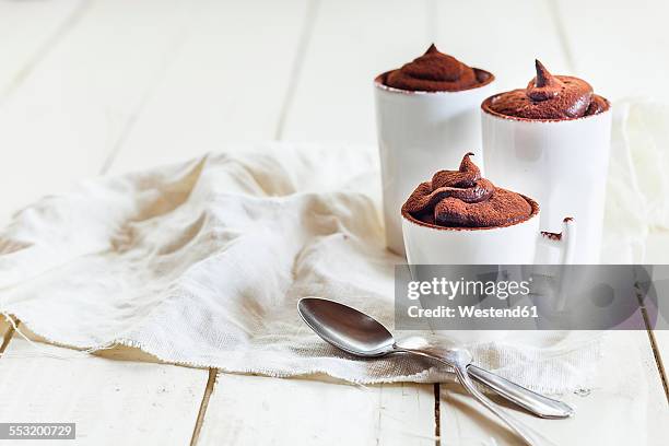 three cups of vegan mousse au chocolat, tea spoons, cloth on white wood - dark chocolate mousse stock pictures, royalty-free photos & images