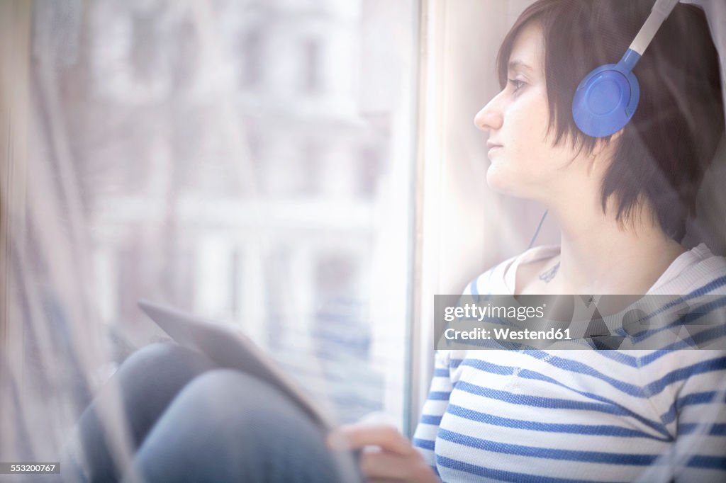 Young woman with headphones and digital tablet looking through window