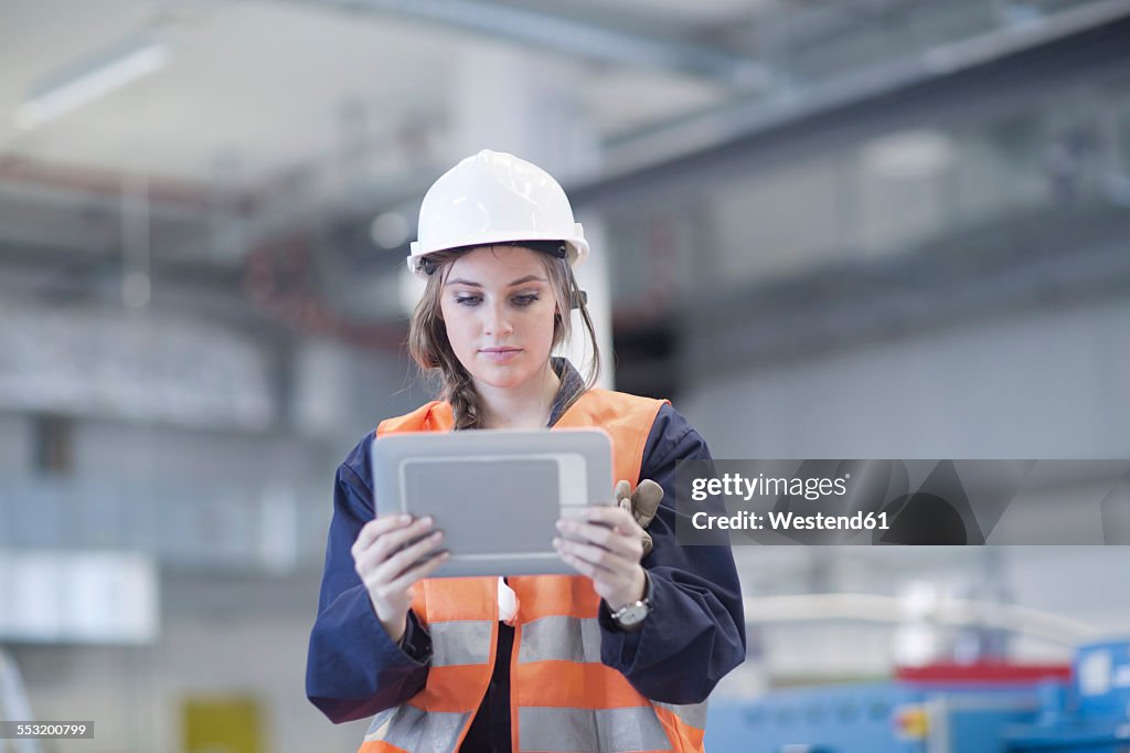 Technician with reflective vest in factory hall using digital tablet