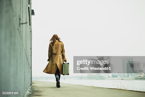 Young woman with suitcase walking by the riverside Young woman with suitcase walking by the riverside