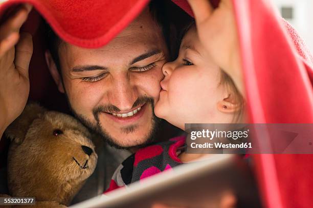 father and daughter with digital tablet under blanket - verwöhnen stock-fotos und bilder