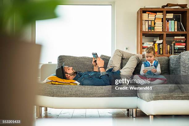 father and daughter with digital tablet and smartphone on sofa - mann handy couch stock-fotos und bilder