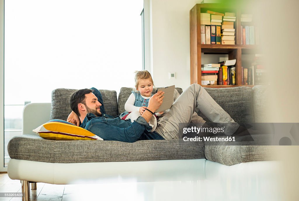 Father and daughter with digital tablet on sofa