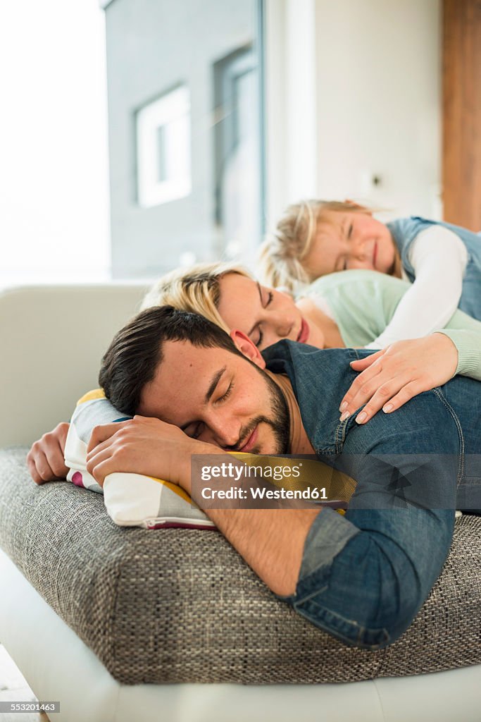 Family lying on couch on top of each other with closed eyes
