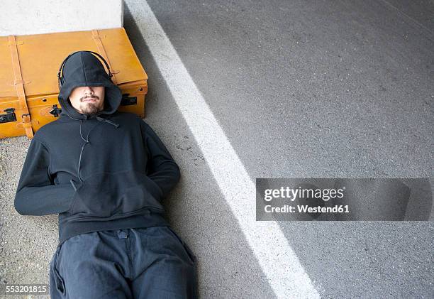 man wearing hooded jacket sleeping beside lane - escapismo foto e immagini stock