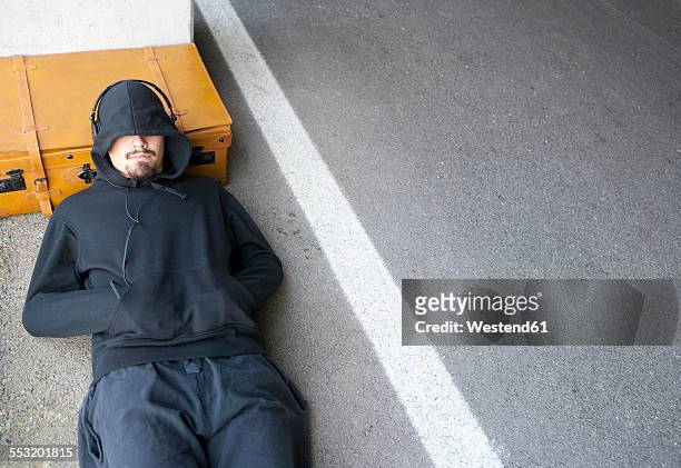 man wearing hooded jacket sleeping beside lane - escapismo imagens e fotografias de stock