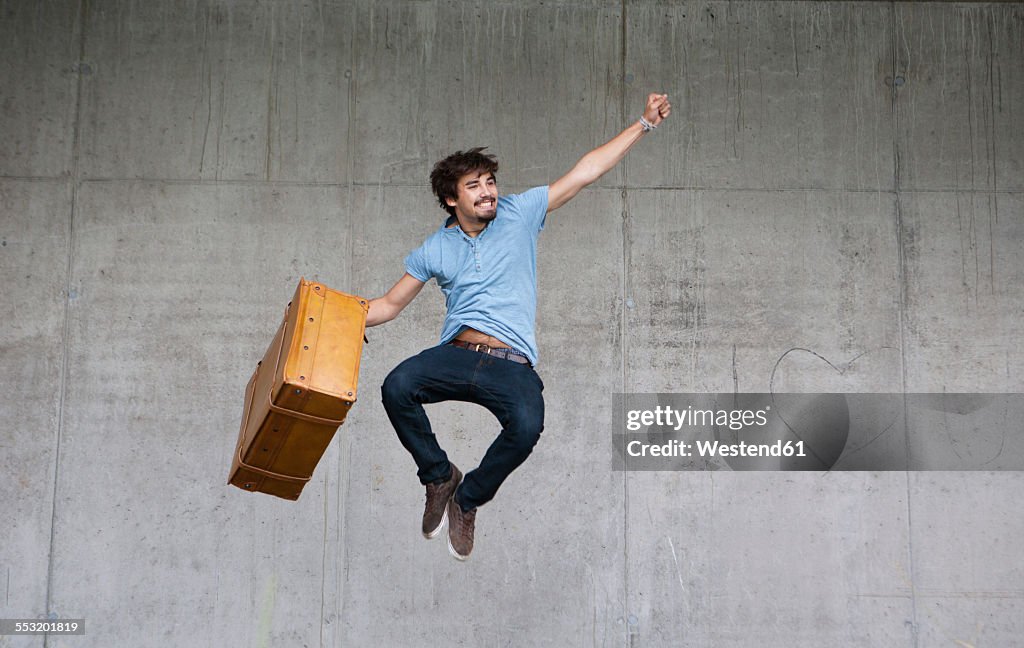 Happy man with leather suitcase jumping in the air