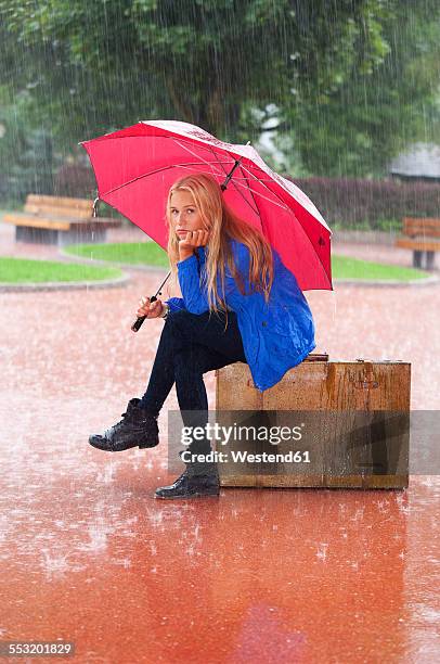 austria, thalgau, teenage girl with red umbrella sitting on her suitcase in the rain - girl wet casual clothing stock pictures, royalty-free photos & images