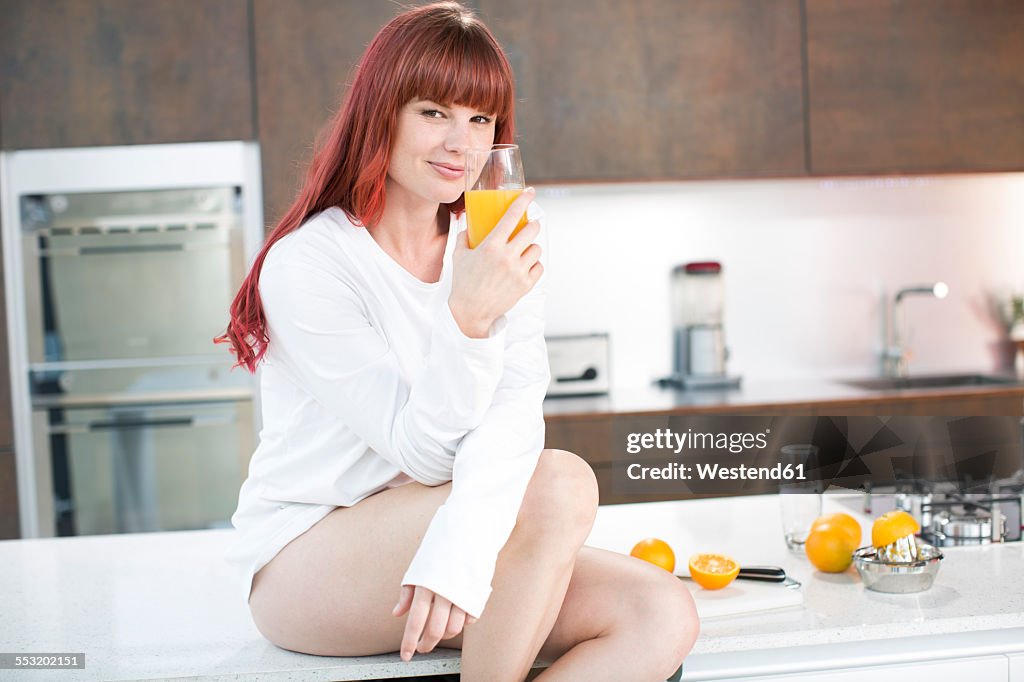 Woman sitting on kitchen counter with fresh made orange juice