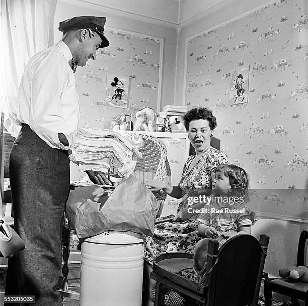 Delivery man for Crib Diaper Service delivers a set of cloth diapers to a mother and her two young children, Long Island, New York, June 1947.