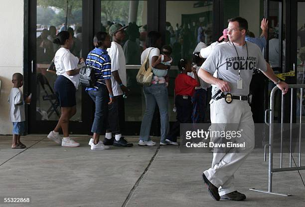 Under the watchful eye of a federal agent, evacuees line up to receive their FEMA debit cards at Reliant Arena, near the Astrodome September 9, 2005...
