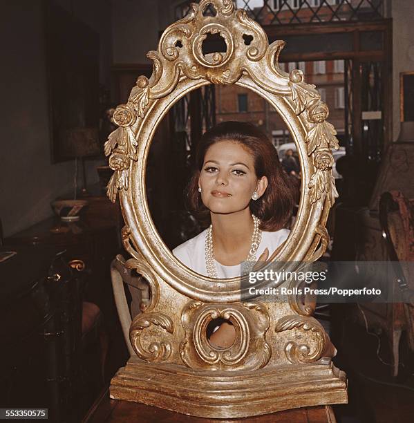 Sicilian actress Claudia Cardinale poses in the centre of a large gilt mirror frame in an antiques shop in Italy in 1965.