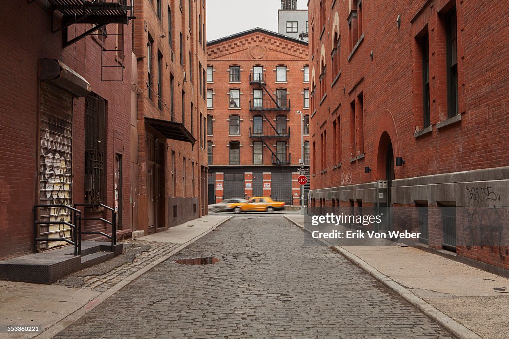 Cobblestone Alley in tribeca with taxi passing by