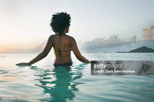 Young black woman wading into ocean, rear view.
