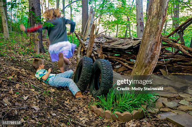 a girl jumps over a boy at their make shift hut in the woods at pittsburgh pa. during the spring - molly steinwald stock pictures, royalty-free photos & images