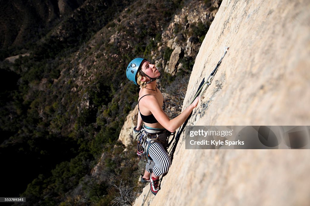 A woman wearing a red tank top and striped pants climbs The Rapture (5.8) on Lower Gibraltar Rock in Santa Barbara, California.