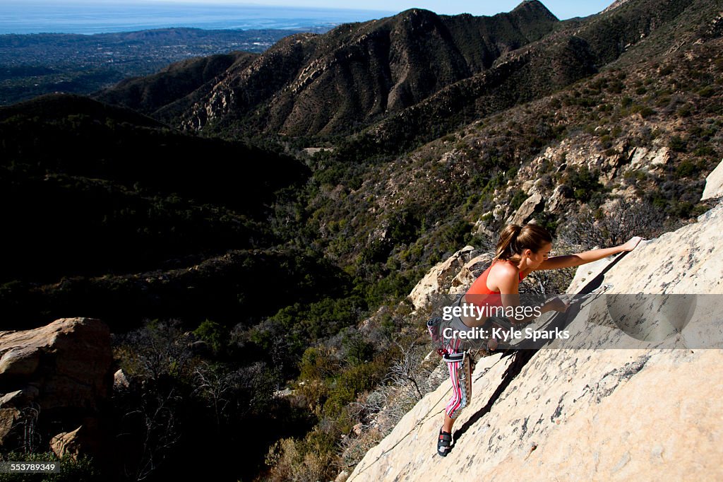 A woman wearing a red tank top and striped pants climbs The Rapture (5.8) on Lower Gibraltar Rock in Santa Barbara, California.
