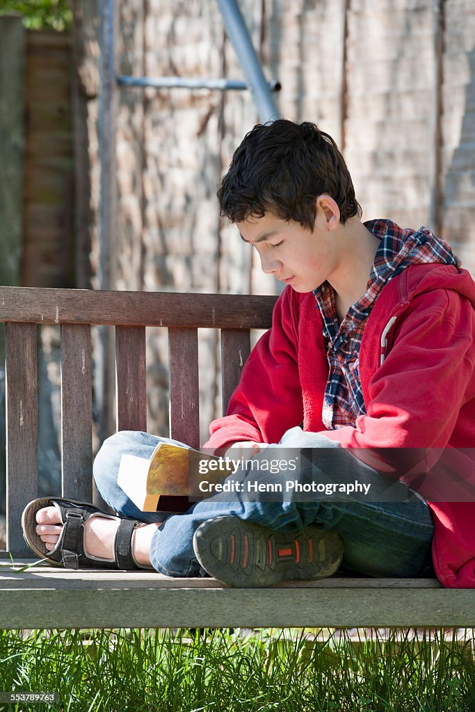 Teenage boy reading a book on a swing in the garden