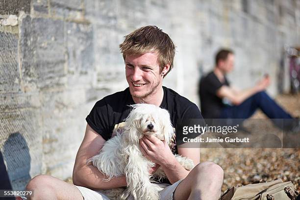 mid 20's male sat on the beach with a puppy - chinese crested powderpuff stock pictures, royalty-free photos & images