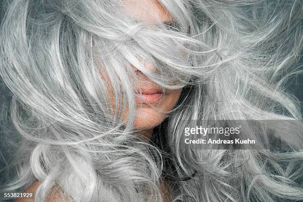 woman with grey hair blowing across her face. - hairstyle stock-fotos und bilder