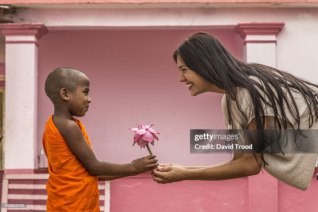 Young Buddhist monk giving lotus flower to tourist