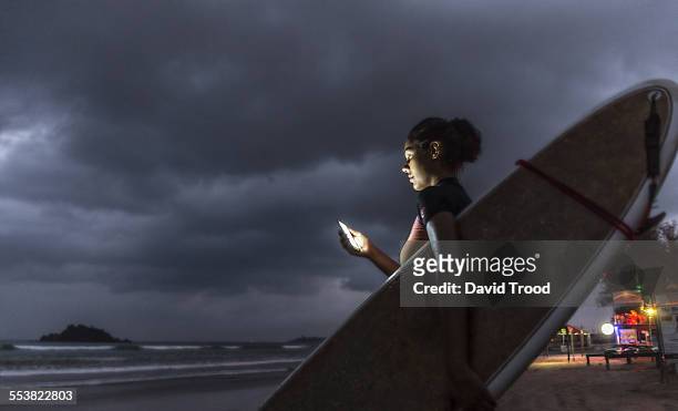 young woman surfer using smart phone at dusk. - beach hold surfboard stock-fotos und bilder